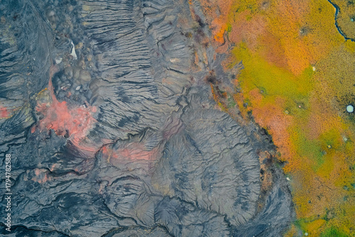 Abstract high-angle drone shot capturing the stark boundary between gray, heavily eroded industrial terrain with a reddish-orange acidic pocket and vibrant yellow and green autumn marshland