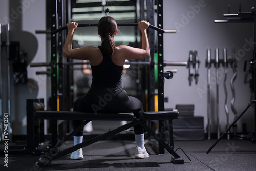 Strong woman lifting weights in a gym during evening workout session for fitness improvement and strength training