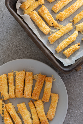 Homemade cheese sticks on baking tray and plate top view