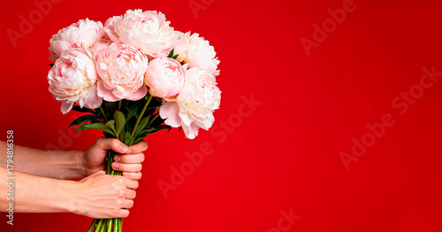 Bouquet of pink peonies in men's hands, on a bright red background. The image has an empty space for text, which is perfect for banners or ads.