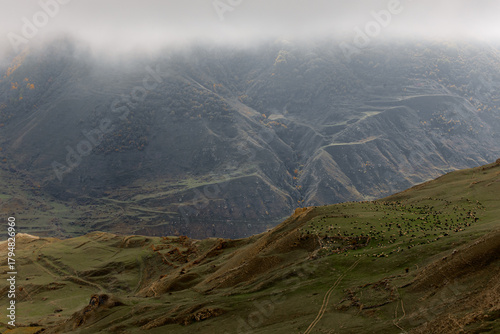 Panoramic view of the mountainous landscape. Rolling hills covered in green grass under a cloudy sky. The terrain is rugged and dramatic.