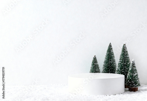 A white podium surrounded by miniature fir trees with lights. The scene is set on a snowy surface, creating a festive atmosphere for product advertising.