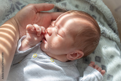 Newborn baby sleeping in sunlight while holding parents hand