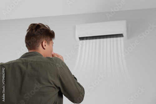 Fotografija Young man suffering from bad smell from air conditioner and covering his nose in