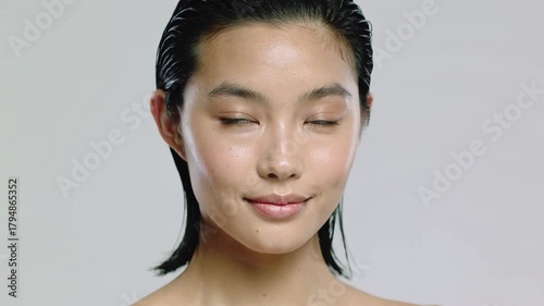 Beauty slow motion video of beautiful young professional asian female model with natural dew skin and slicked-back  black wet hair, posing with hands and light smile on her face.Macro.AI Generative.
