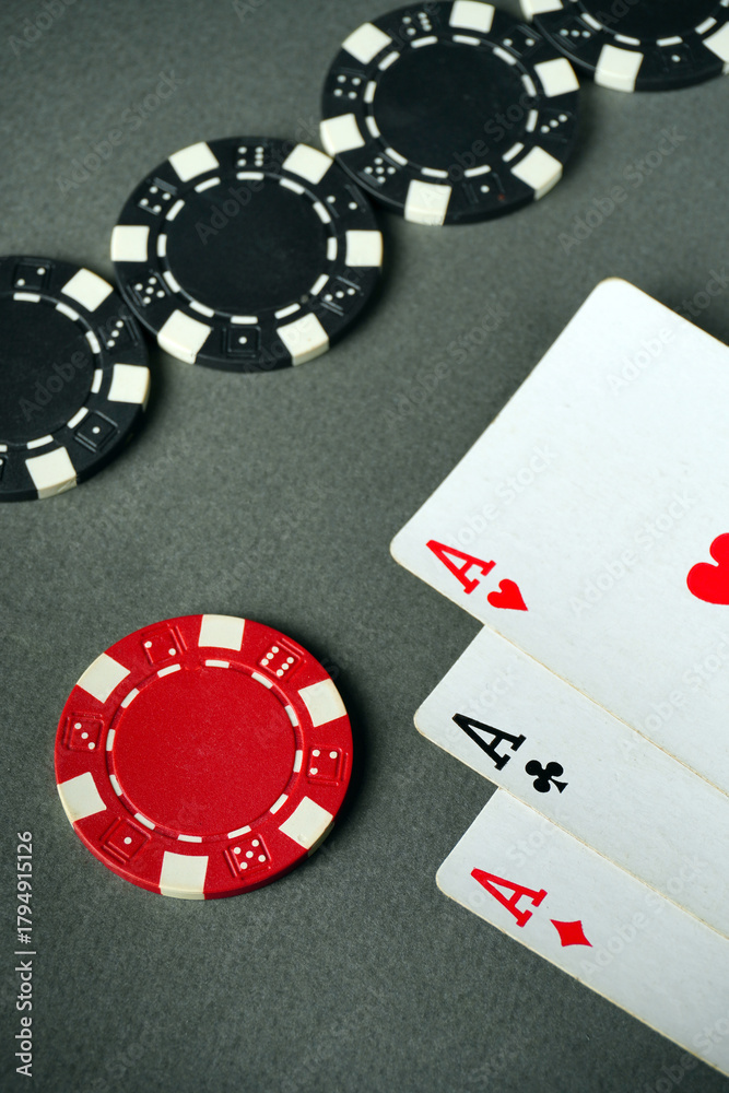 Obraz premium Players are engaged in a game of poker, showcasing three aces and various chips on a gray table. The scene captures the excitement and strategy involved in card games