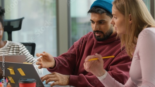 Pensive thinking Arabian informal business man Indian male worker startup founder working with laptop typing writing notes in office casual businessman job concentrated with two multiracial women