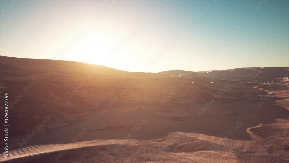Naklejka premium Bright sunlight glimmers across the expansive desert, illuminating the soft dunes and rugged hills. The serene atmosphere captures the beauty of a new day in nature, inviting peaceful reflection.