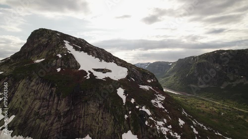 Aerial view of a serene lake nestled between rugged mountains, where patches of snow meet lush greenery under a cloudy sky, Dalen, Telemark, Norway.