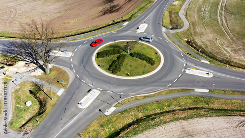 Aerial view of a rural roundabout with cars navigating circular intersection, surrounded by fields and sparse trees