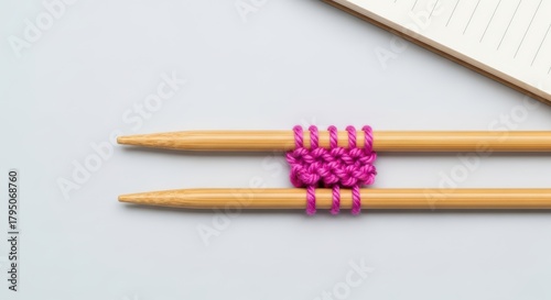 Pink yarn on bamboo knitting needles with notebook on white background
