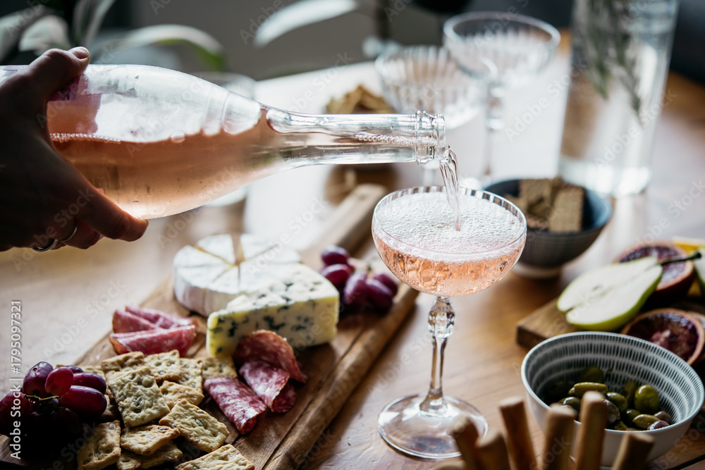Naklejka premium Pouring rose wine with classic snacks of cheese, bread and olives. Party or anniversary celebration.