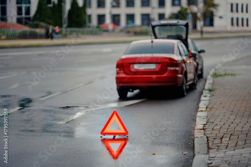 Emergency warning triangle placed behind vehicle after minor rear end collision on wet city road during evening traffic, road safety precautions and hazard signaling for approaching motorists