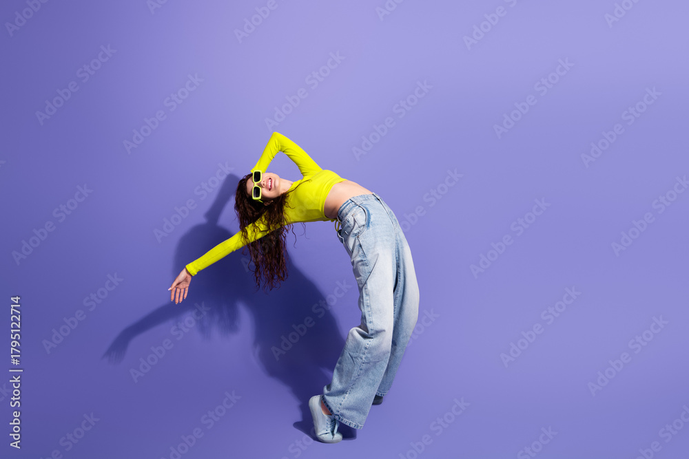 Naklejka premium Young woman in neon yellow top posing and stretching against a purple studio background fashion lifestyle model