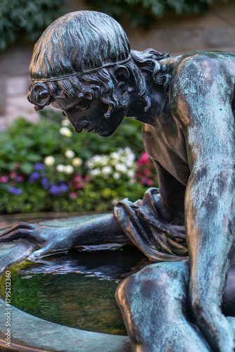 Bronze sculpture of Narcissus admiring his reflection in the courtyard of Cecilienhof Palace, Potsdam. Artistic depiction of Greek mythology in a historic setting.