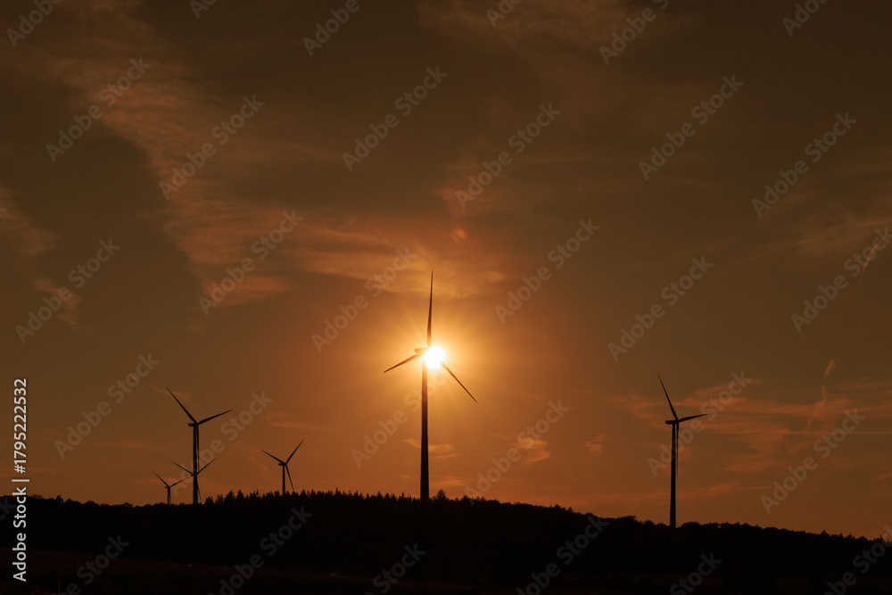 Obraz premium Wind turbines in sunset light creating a dramatic silhouette, symbolizing renewable energy, sustainability, and the future of clean power.