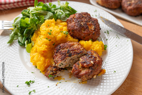 Homemade german meatballs with mashed pumpkin potatoes and a green salad on a plate. Delicious winter food