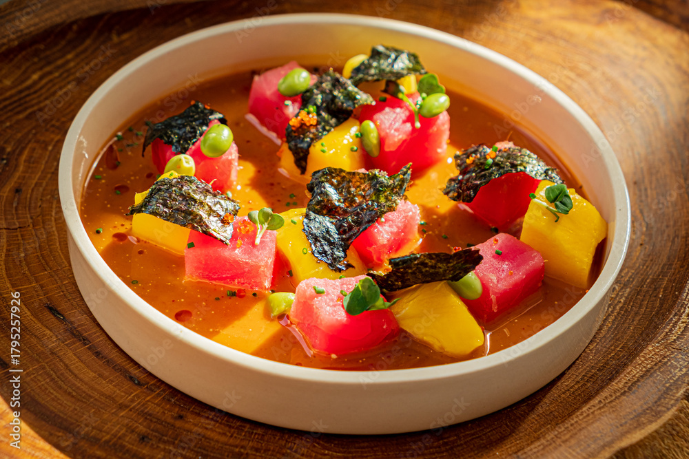 Fototapeta premium Fresh watermelon, mango, and avocado cubes complemented by a rich broth and seaweed