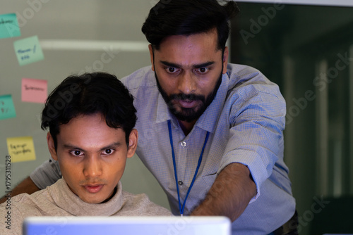 Business team analyzing data on laptops with growth chart in background. Diverse professionals collaborating in office, discussing financial performance, strategy, and success analytics in workplace.