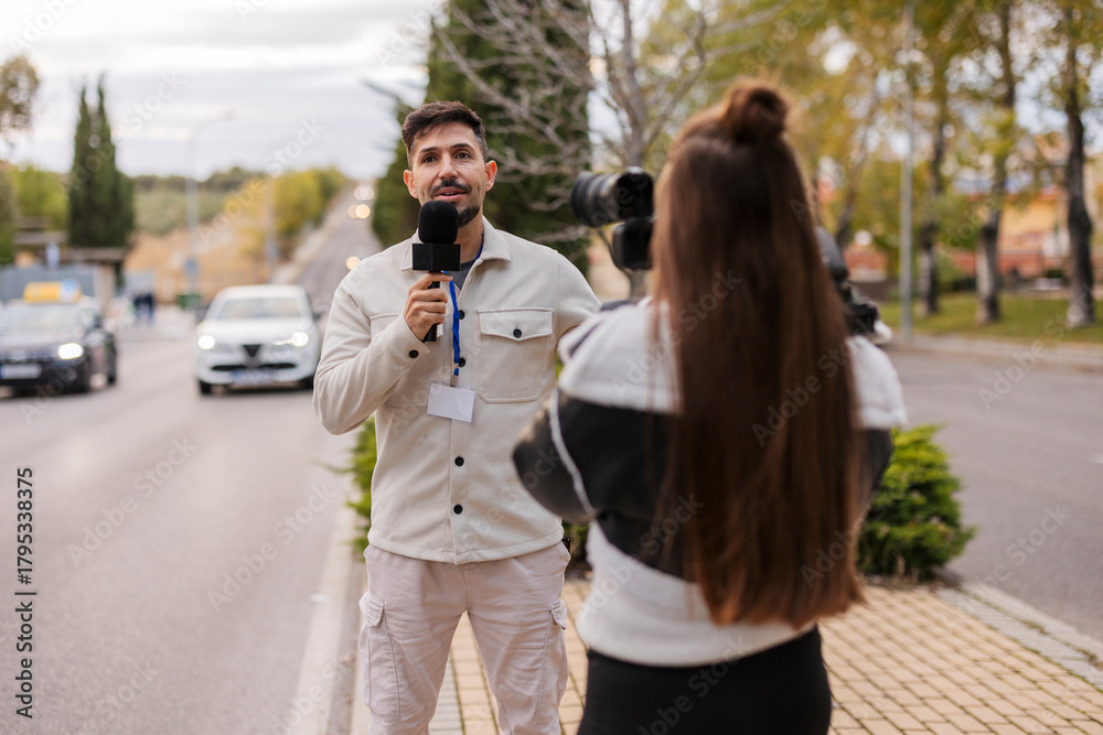 Fototapeta premium Male reporter speaking into microphone with camerawoman filming