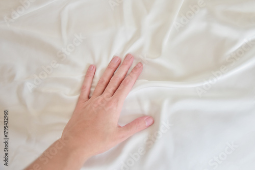 Female hand gently touching white silky sheet