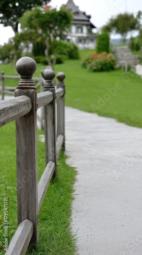 Rustic wooden fence with decorative tops leads to an old house in a serene country setting surrounded by green grass and trees