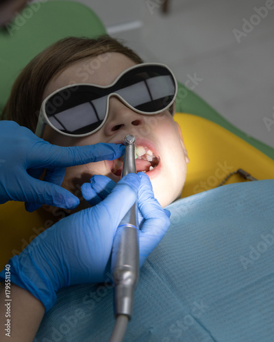 Pediatric dentist treating a young boy’s teeth with a dental hand piece in a modern clinic