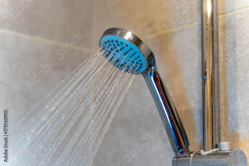 Modern showerhead with water flowing down, showcasing sleek design and functionality, set against a textured bathroom wall, emphasizing relaxation and cleanliness