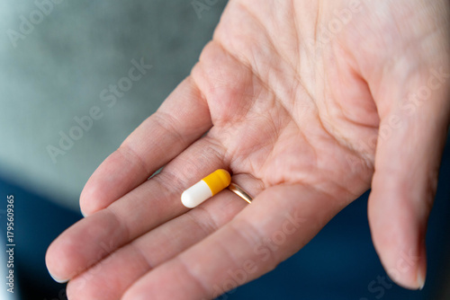 Photos Hand of a person holding a yellow and white capsule pill, showcasing the importa
