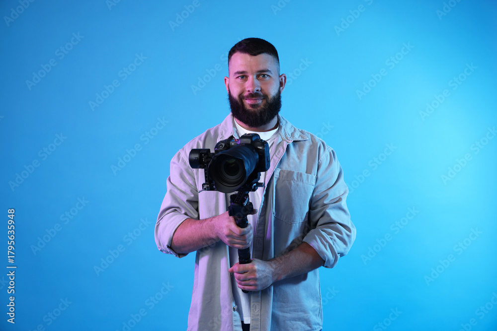 Obraz premium Videographer using gimbal stabilizer with camera on light blue background