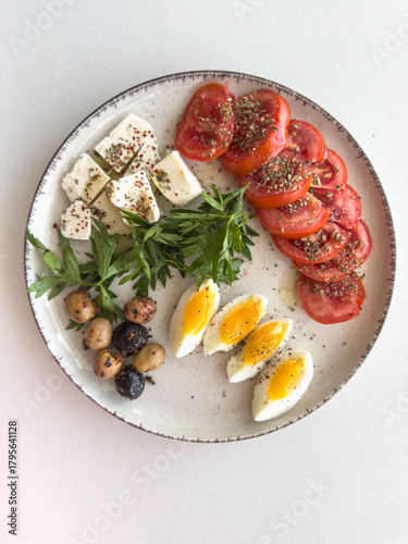 breakfast plate with boiled egg, tomato, cheese, olives and herbs