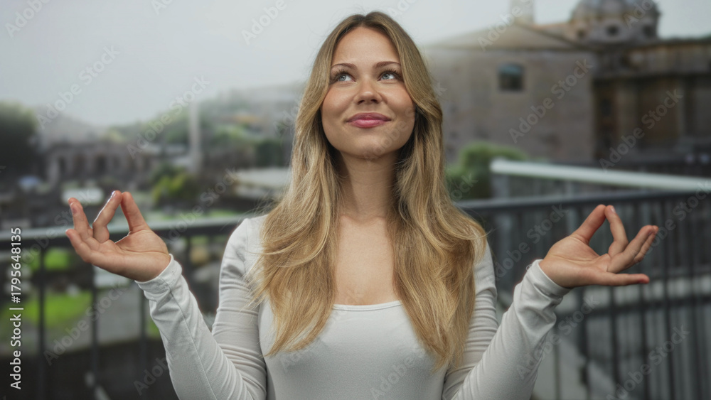 Fototapeta premium Woman with blonde hair and hands in mudra gesture meditating on a balcony; serenity mindfulness calm.
