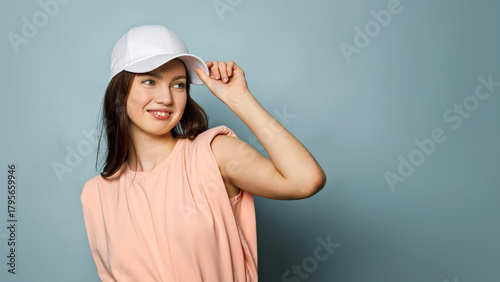 Young woman wearing a white cap poses cheerfully against a blue background