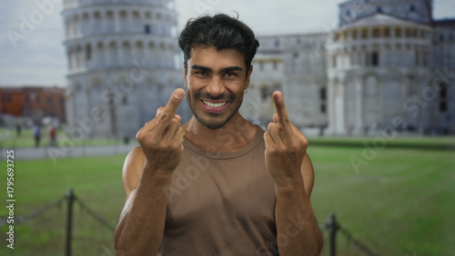 Man in brown tank top shows middle finger gesture at pisa tower building; defiance rebellion attitude.
