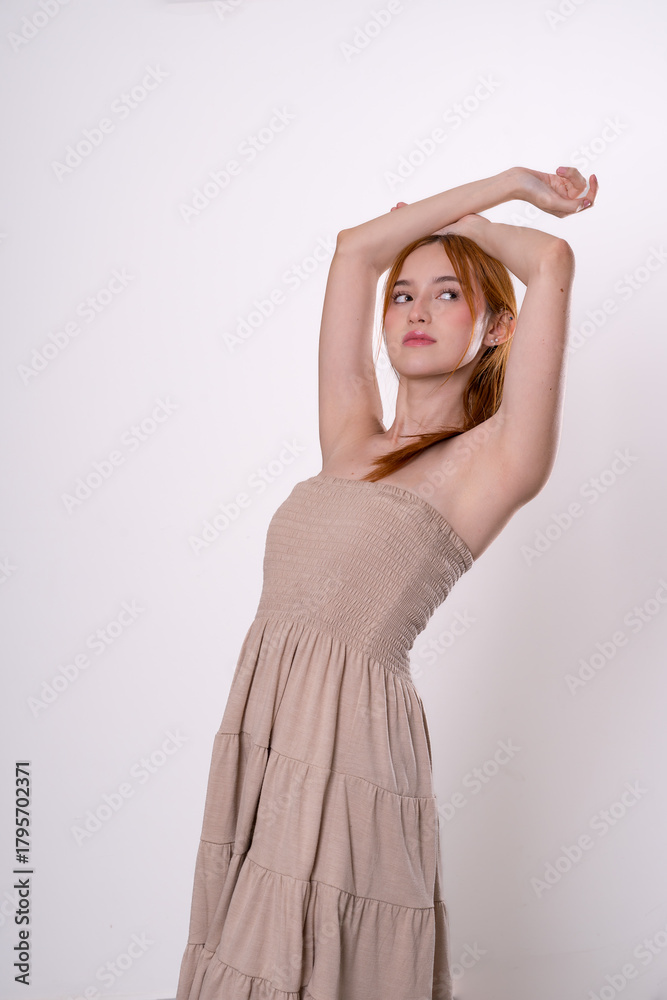 Fototapeta premium Red-haired woman posing with raised arms and bright smile, confident studio portrait.