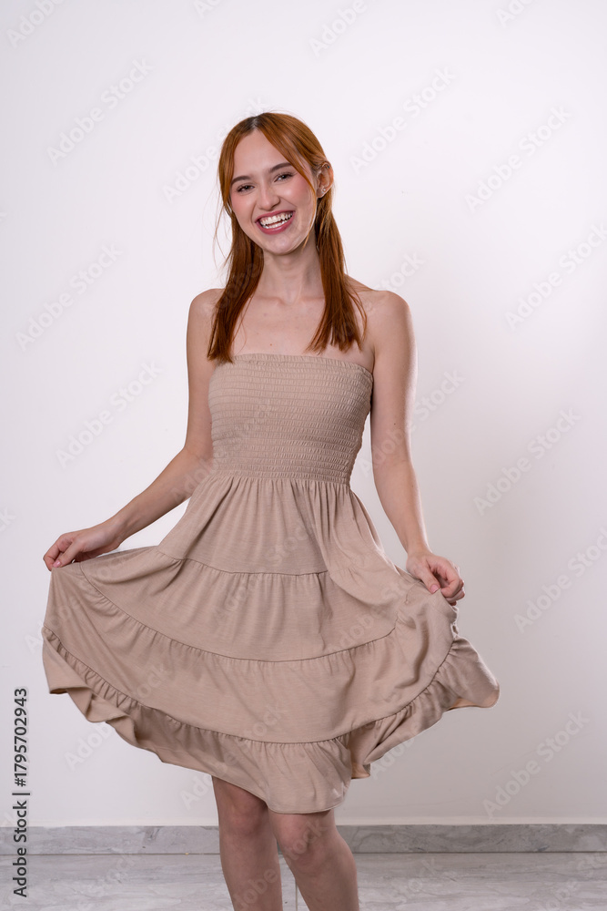 Naklejka premium Red-haired woman smiling while holding dress, minimal and charming studio portrait.