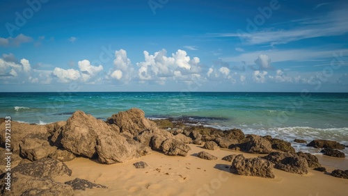 Scenic beach with rocks, sandy shore, and blue ocean under a partly cloudy sky