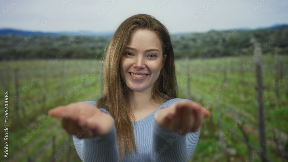 Obraz premium Woman holds out open palms and smiles in a green countryside vineyard; compassion generosity hope acceptance.