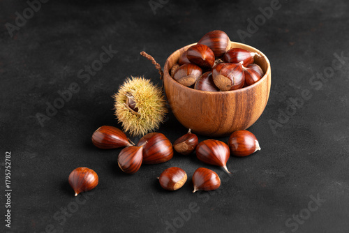 Fresh chestnuts in a rustic wooden bowl set on black background, creating a warm autumn kitchen mood
