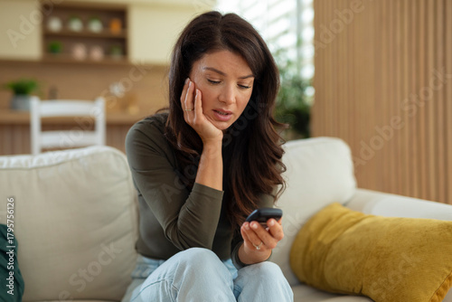 Concerned young woman looking at a glucose meter with a worried expression while checking her blood sugar at home.
