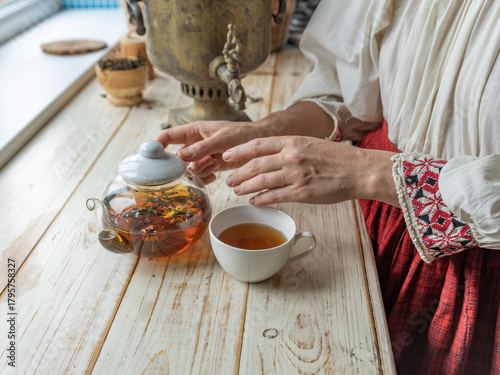 Woman is pouring tea into a cup from a teapot