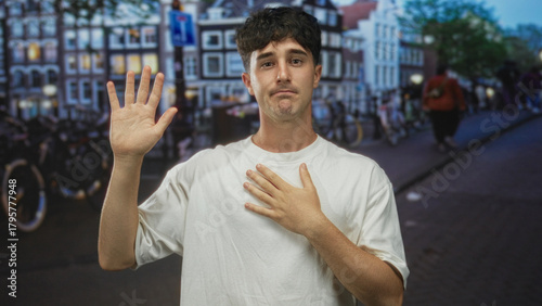 Man raises one hand and places other hand on chest on a street lined with bicycles at dusk; regret apology contrition.
