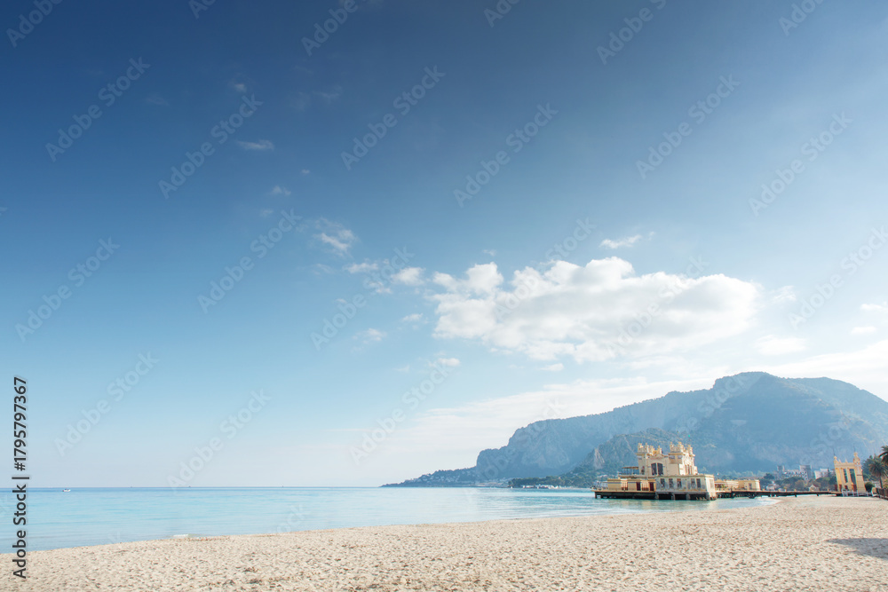 Fototapeta premium Sunny Beach With Clear Water And Mountain Backdrop Featuring A Small Pier Building