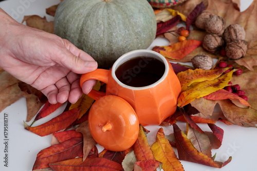 Hand holding a cup of coffee and autumn leaves.