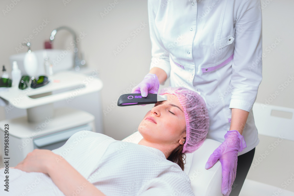 Obraz premium Hands of cosmetologist making ultrasound facial cleaning with special machine