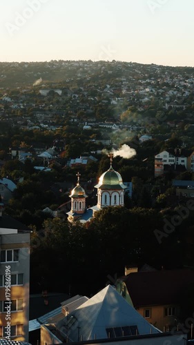 Church and city view time-lapse.
Cityscape with a historic church featuring domes, surrounded by buildings and captured in gentle evening light from above.