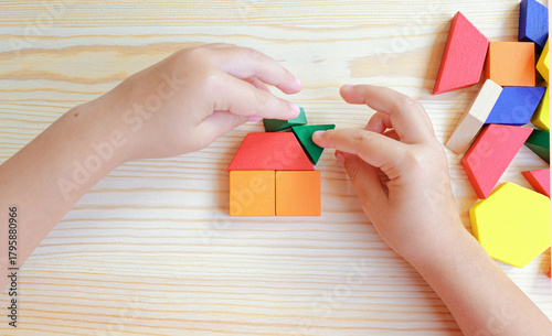 A child's hand constructs a house using multicolored wooden blocks and construction figures. A close-up of multicolored wooden blocks against a wooden table.