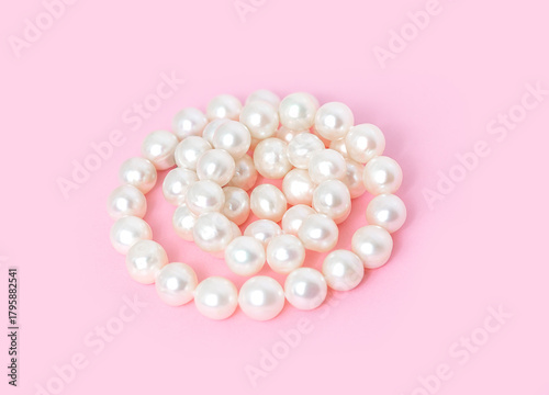 A pearl necklace is twisted into a circle on a soft pink background for Valentine's Day use.