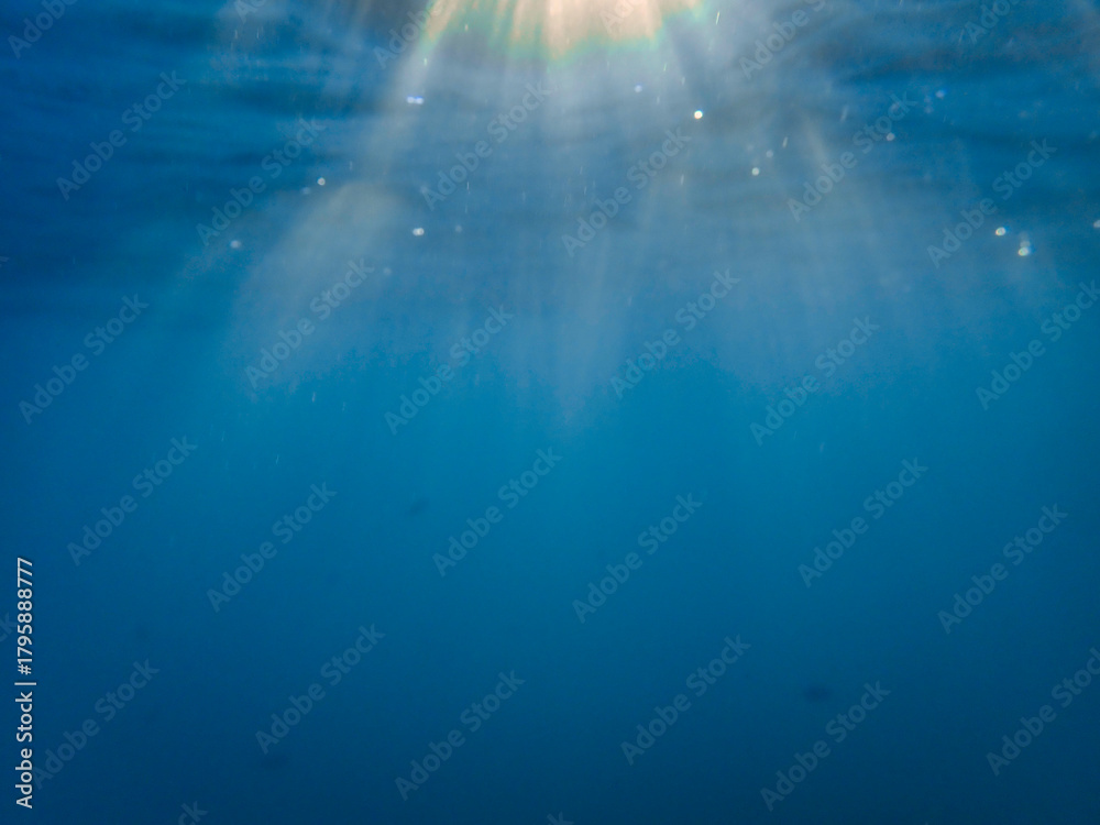 Obraz premium Dark blue ocean surface seen from underwater. Abstract waves underwater and rays of sunlight shining through, Sun light rays undersea deep, Underwater background with sea bottom, Mediterranean sea.