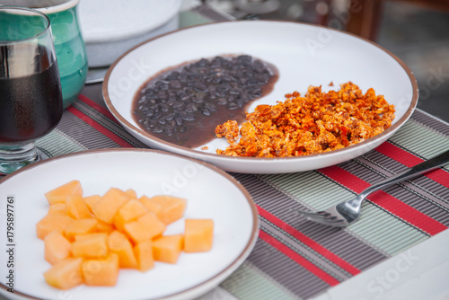 Desayuno huevos con chorizo acompañado por Frijoles y un plato de Melon